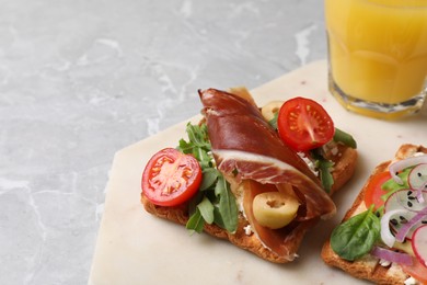 Delicious sandwich with cheese, prosciutto, tomato and arugula on light marble table, closeup