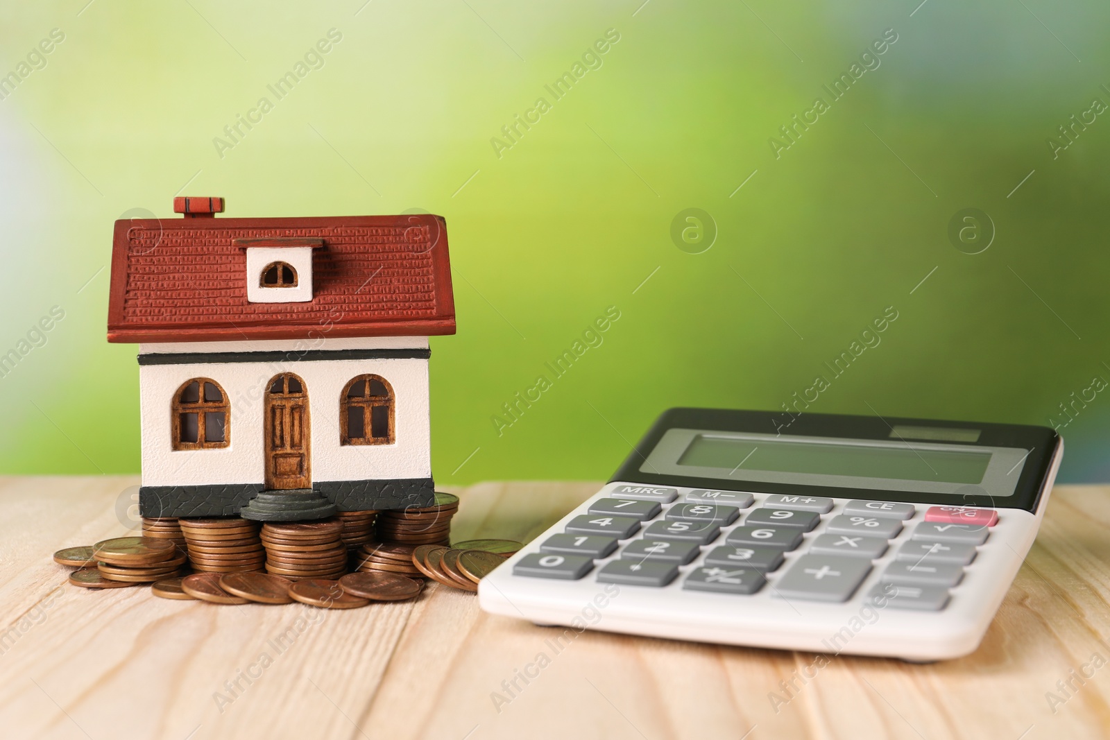 Photo of House model, calculator and coins on wooden table against blurred green background, space for text