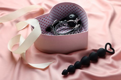 Photo of Heart shaped gift box with different sex toys and ribbon on pink silk fabric