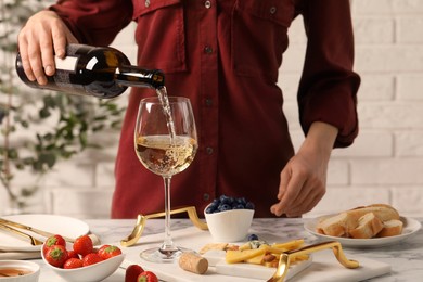 Photo of Woman pouring wine from bottle into glass at table with different snacks, closeup