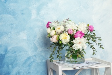 Photo of Vase with bouquet of beautiful flowers on table against color background