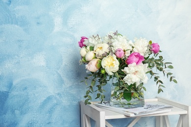 Vase with bouquet of beautiful flowers on table against color background