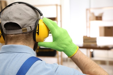 Photo of Worker wearing safety headphones indoors, back view. Hearing protection device