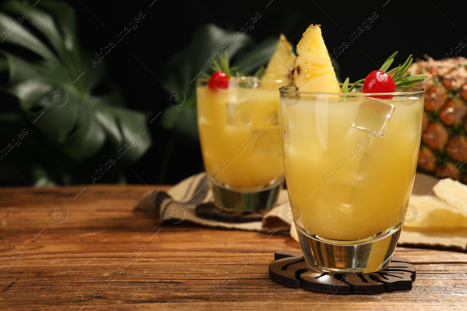 Photo of Glasses of tasty pineapple cocktail with rosemary and cherry on wooden table. Space for text