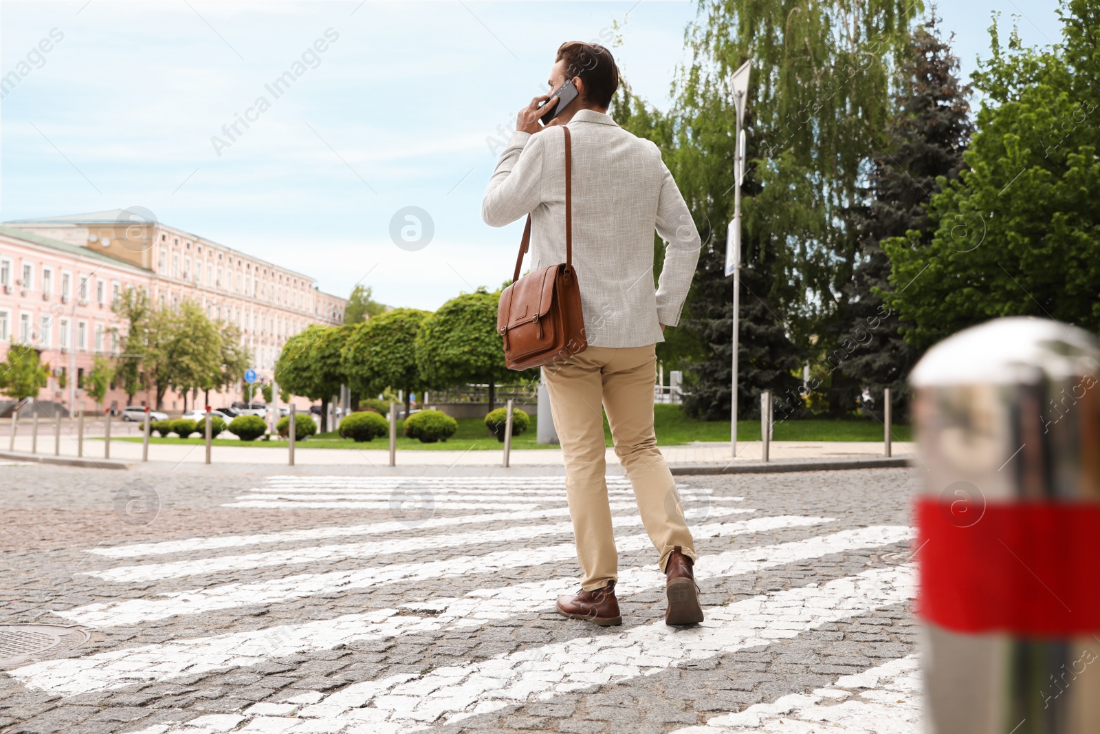 Photo of Young man talking on phone while crossing street, back view. Traffic rules and regulations