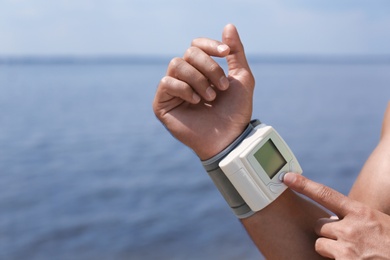 Photo of Young man checking pulse with medical device on beach, closeup. Space for text