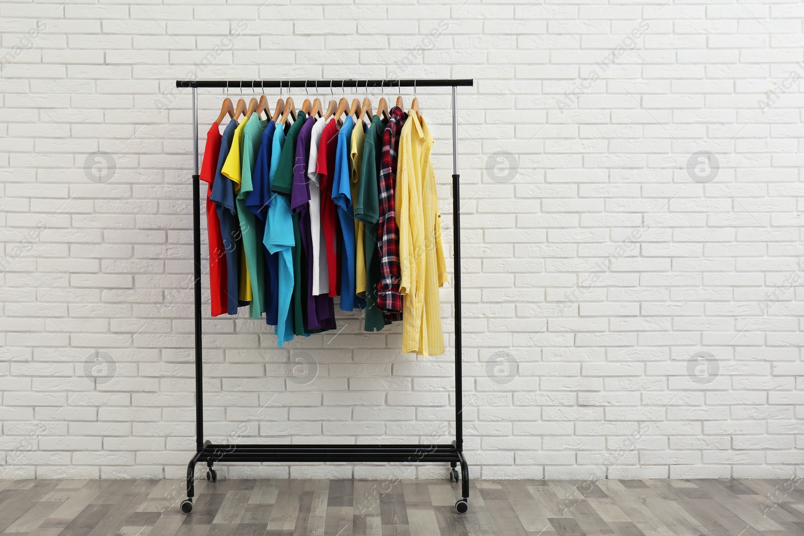 Photo of Rack with stylish clothes near white brick wall. Space for text