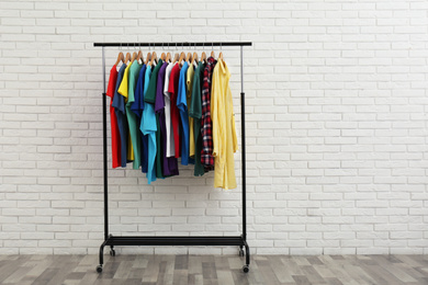 Photo of Rack with stylish clothes near white brick wall. Space for text