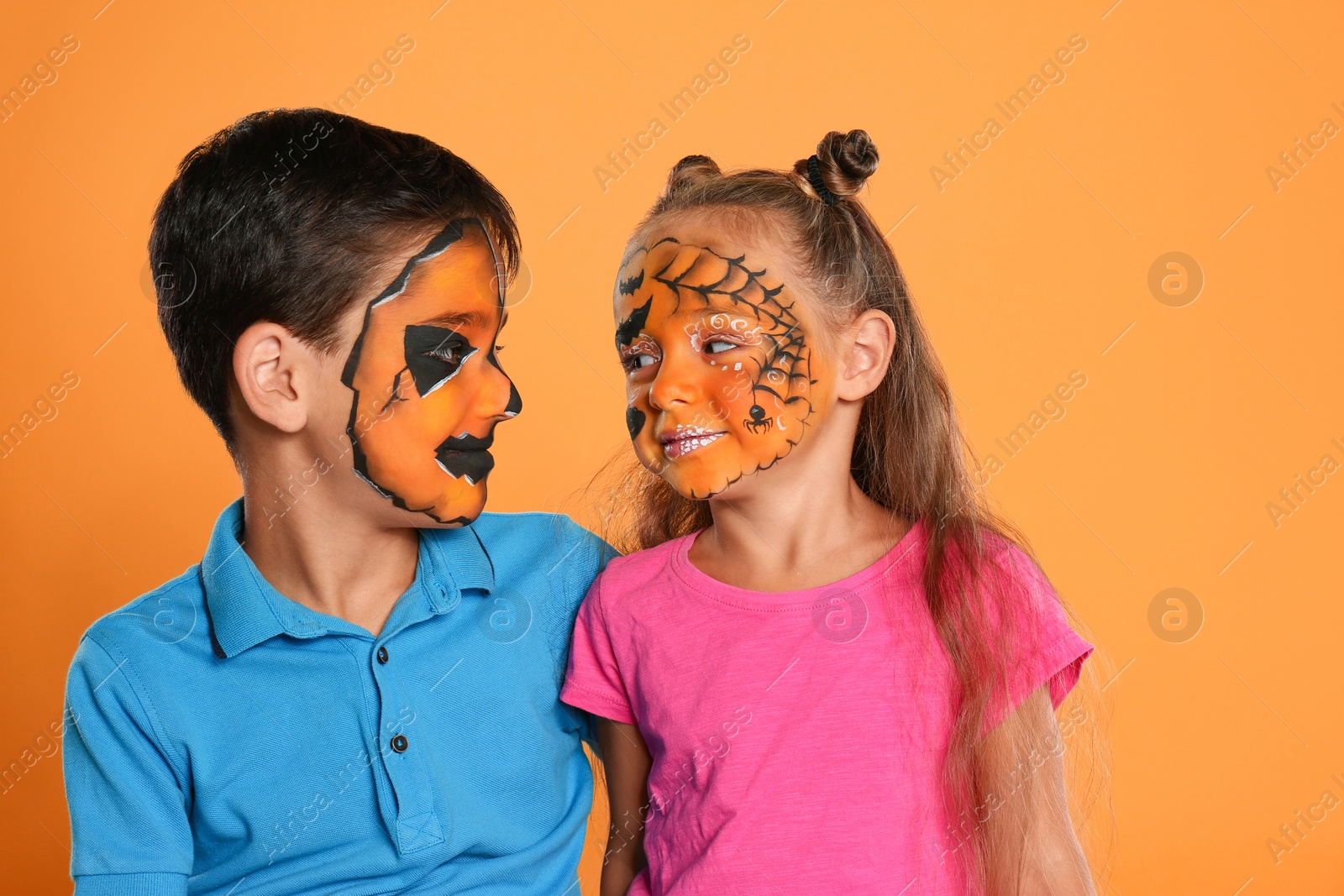 Photo of Cute little children with face painting on orange background