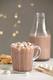 Cup of aromatic hot chocolate with marshmallows and cocoa powder on white table, closeup