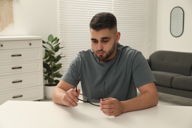 Sad man with glasses sitting at table indoors