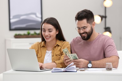 Happy young couple counting money at white table indoors