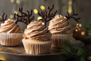 Photo of Tasty Christmas cupcakes with chocolate reindeer antlers on wooden tray, closeup