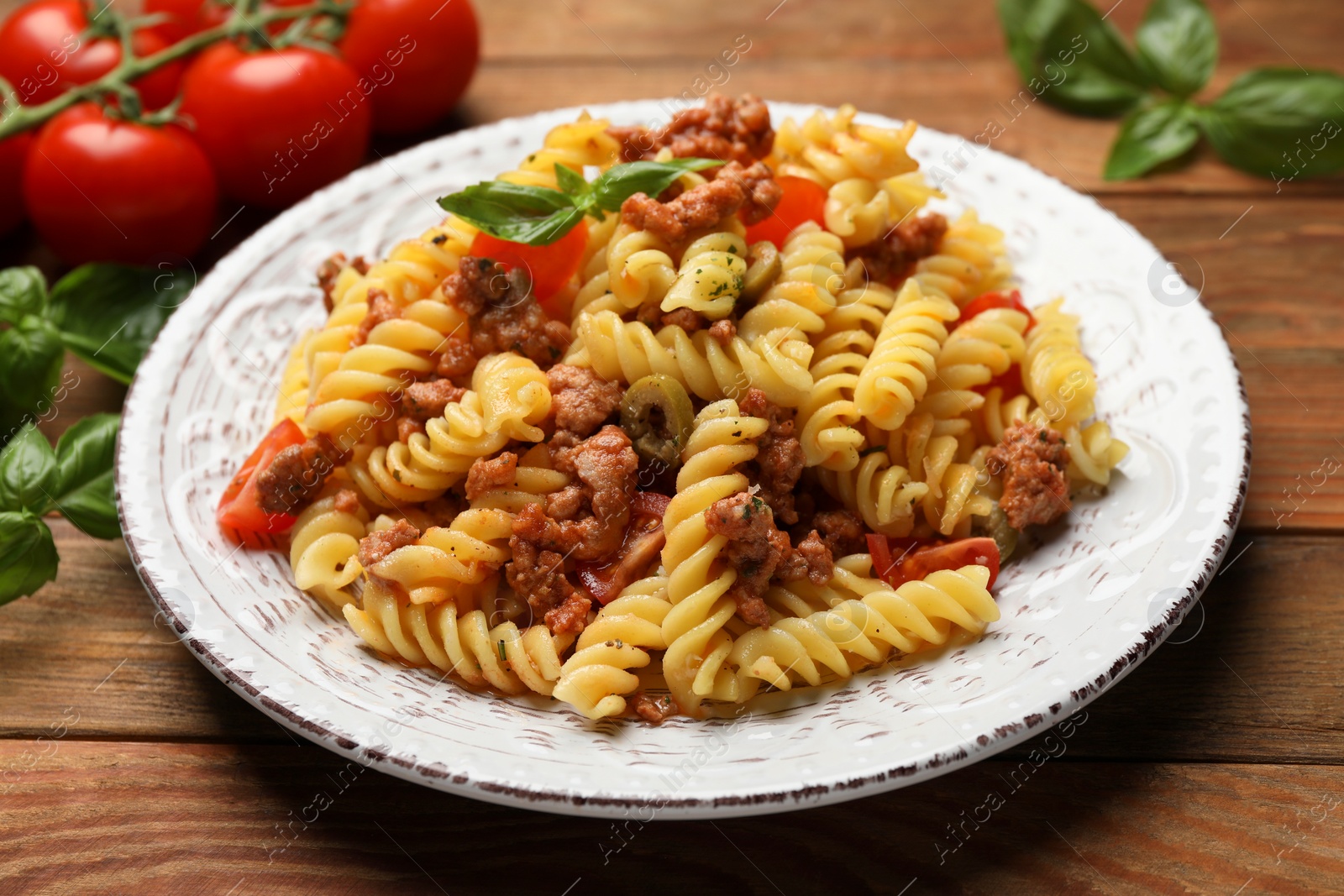 Photo of Plate of delicious pasta with minced meat, tomatoes and basil on wooden table, closeup