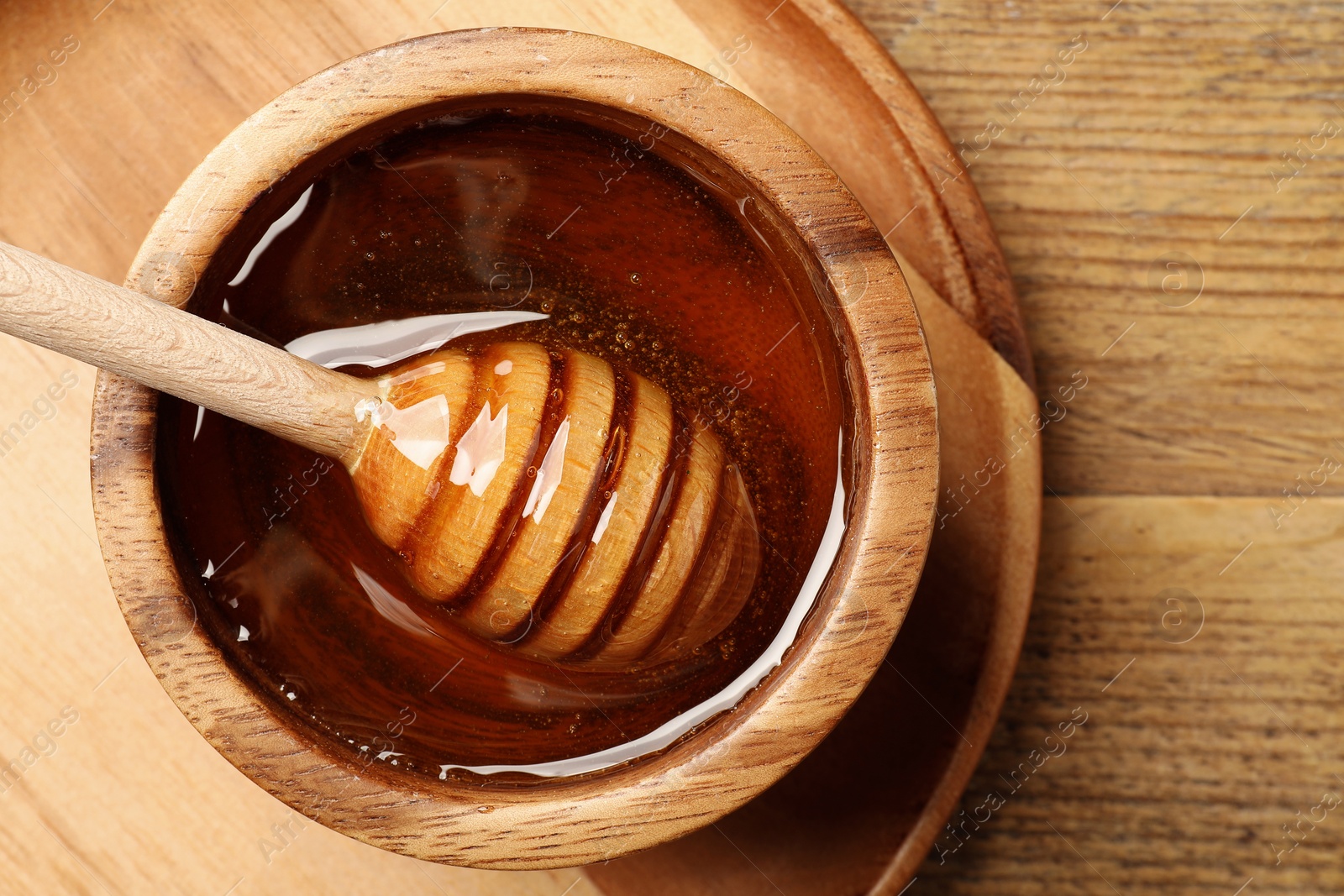 Photo of Dipper with honey in bowl on wooden table, top view. Space for text