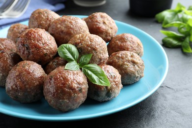 Photo of Tasty cooked meatballs with basil on black table, closeup