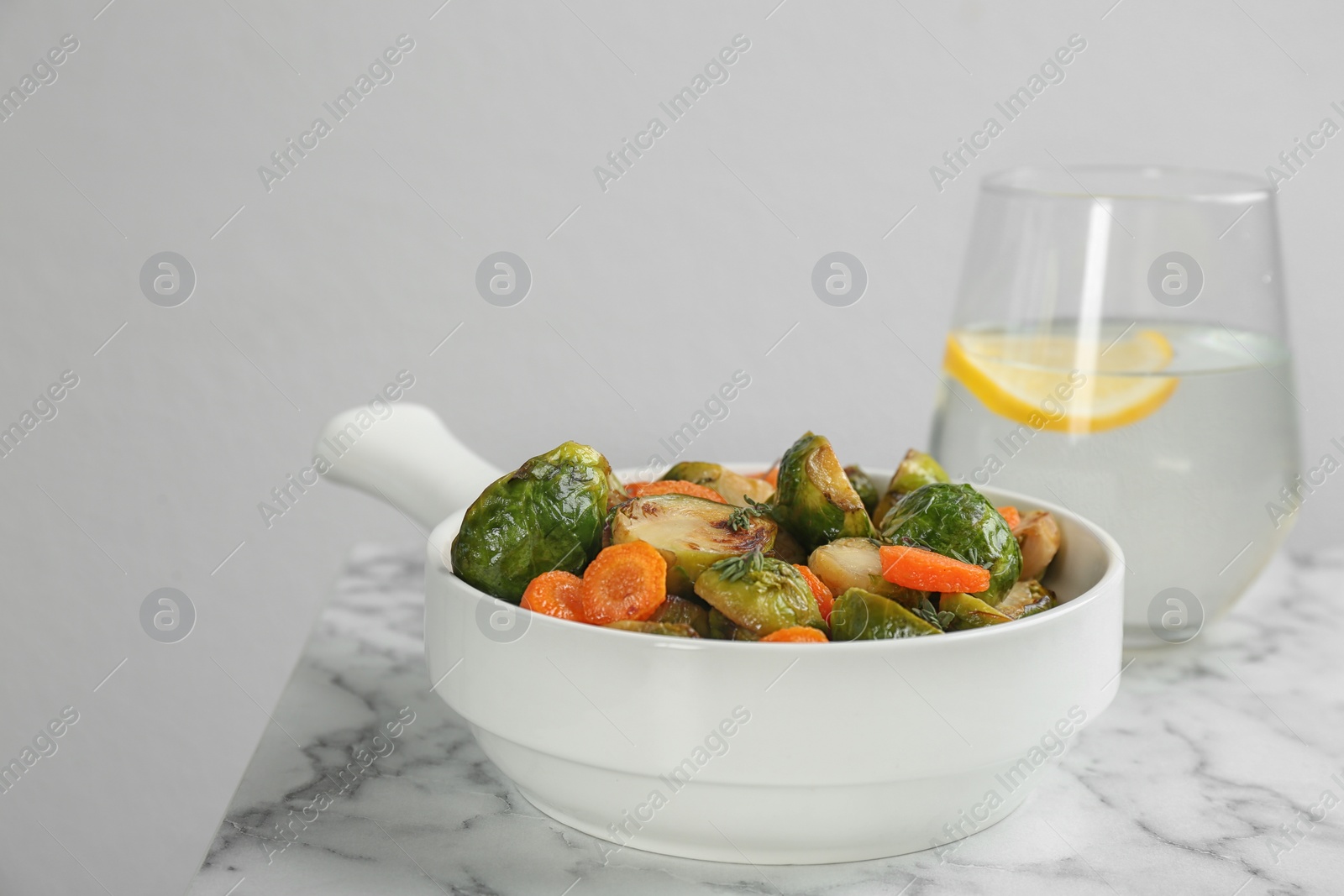Photo of Delicious roasted Brussels sprouts with carrot on white marble table
