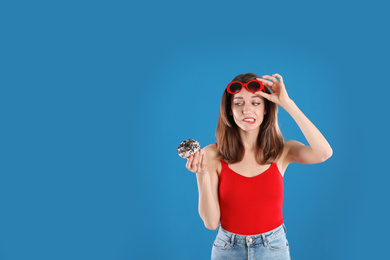 Photo of Beautiful young woman wearing sunglasses with donut on blue background. Space for text