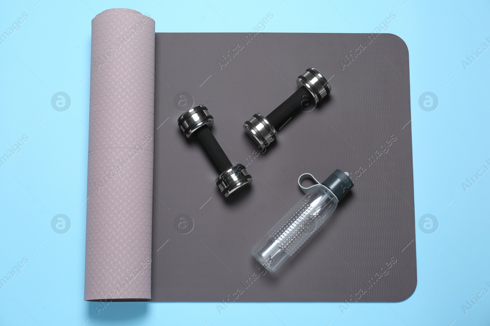 Photo of Exercise mat, dumbbells and bottle of water on light blue background, top view
