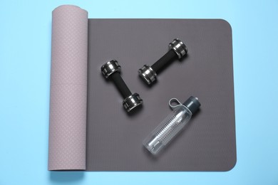 Exercise mat, dumbbells and bottle of water on light blue background, top view