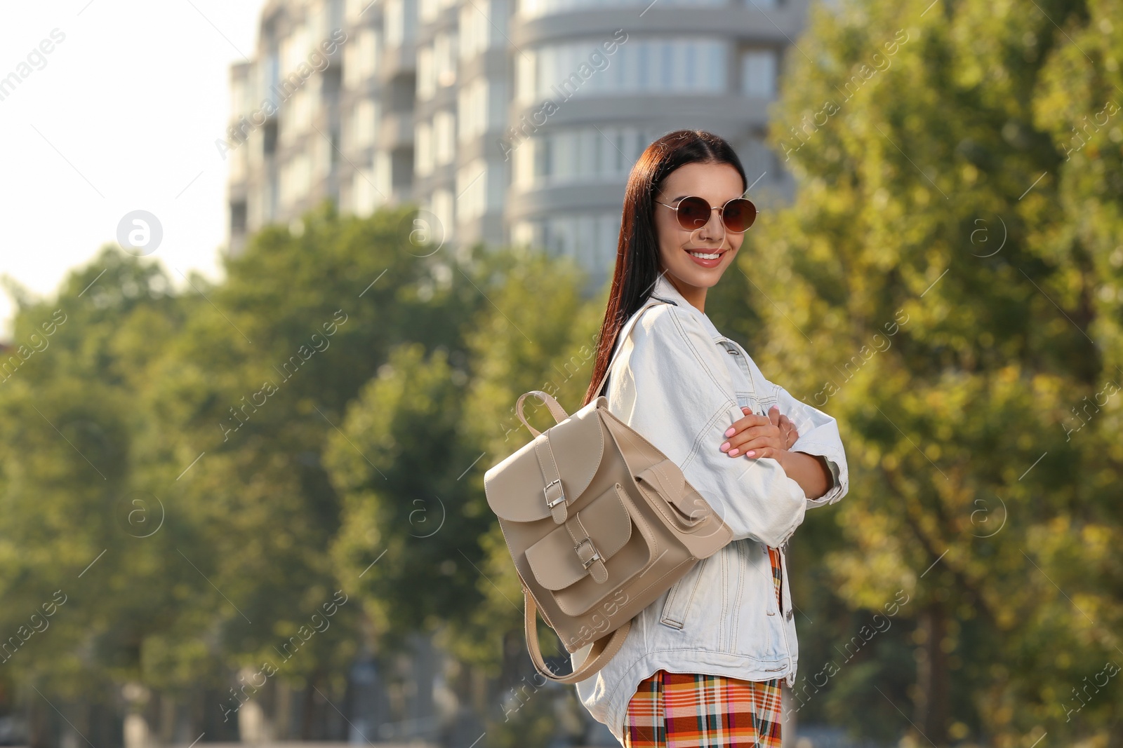 Photo of Beautiful young woman with stylish beige backpack on city street, space for text