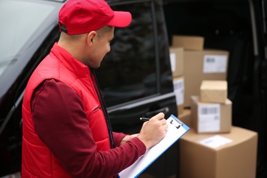 Photo of Courier checking amount of parcels in delivery van outdoors. Space for text