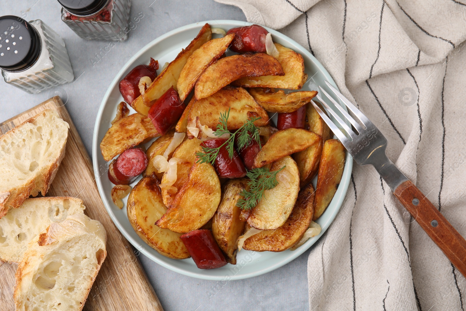 Photo of Delicious baked potato with thin dry smoked sausages served on gray table, flat lay