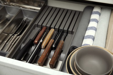 Open drawer of kitchen cabinet with different utensils, dishware and towels, closeup