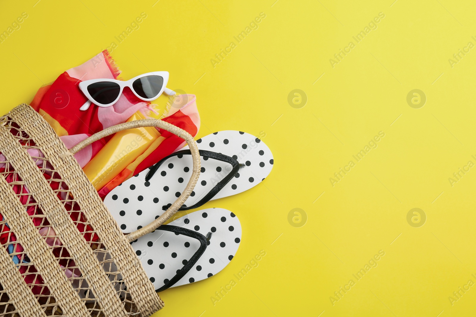 Photo of Bag with beach accessories on yellow background, flat lay. Space for text