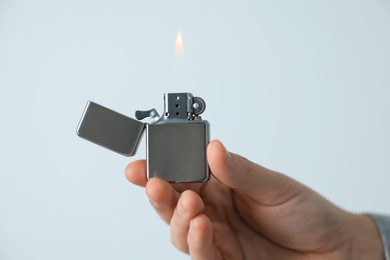Photo of Man holding lighter with burning flame against light grey background, closeup