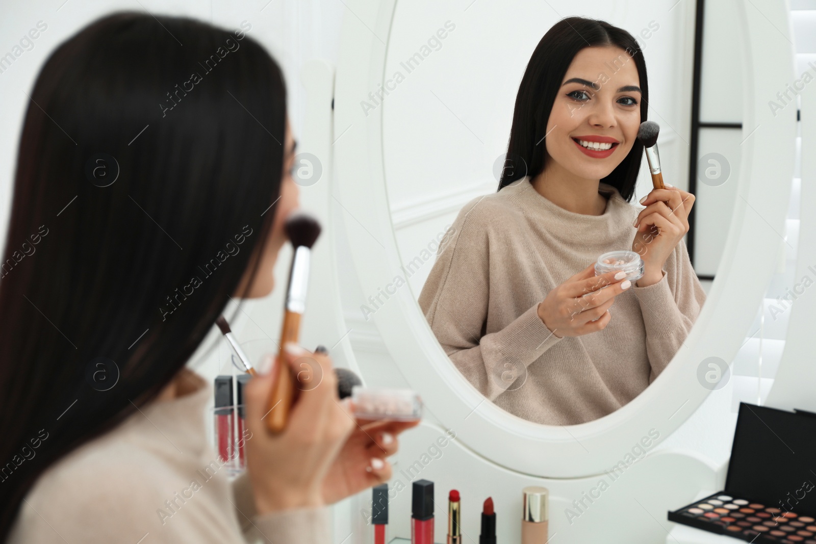 Photo of Beautiful woman applying makeup near mirror in room