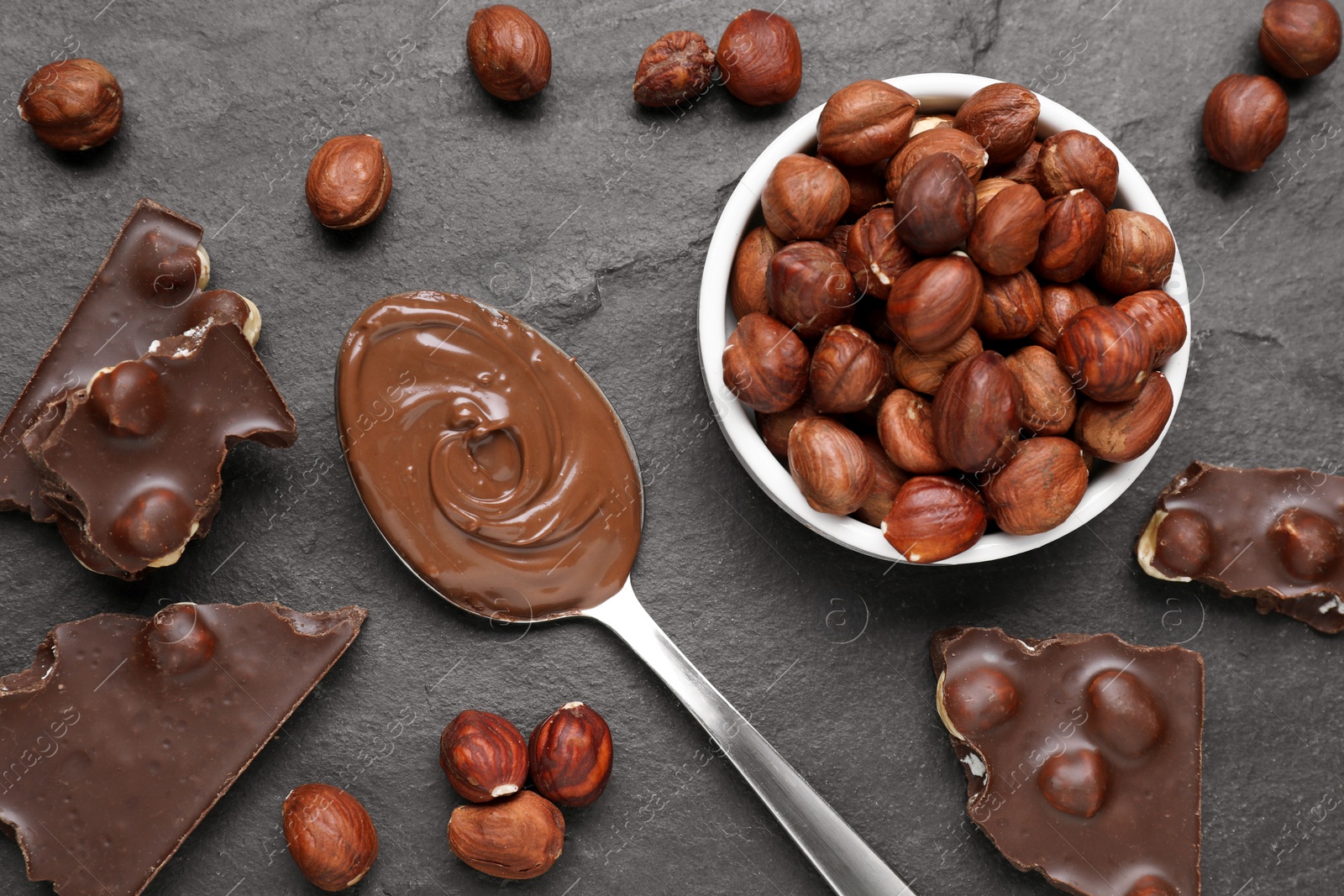 Photo of Spoon with tasty paste, chocolate pieces and nuts on grey table, flat lay