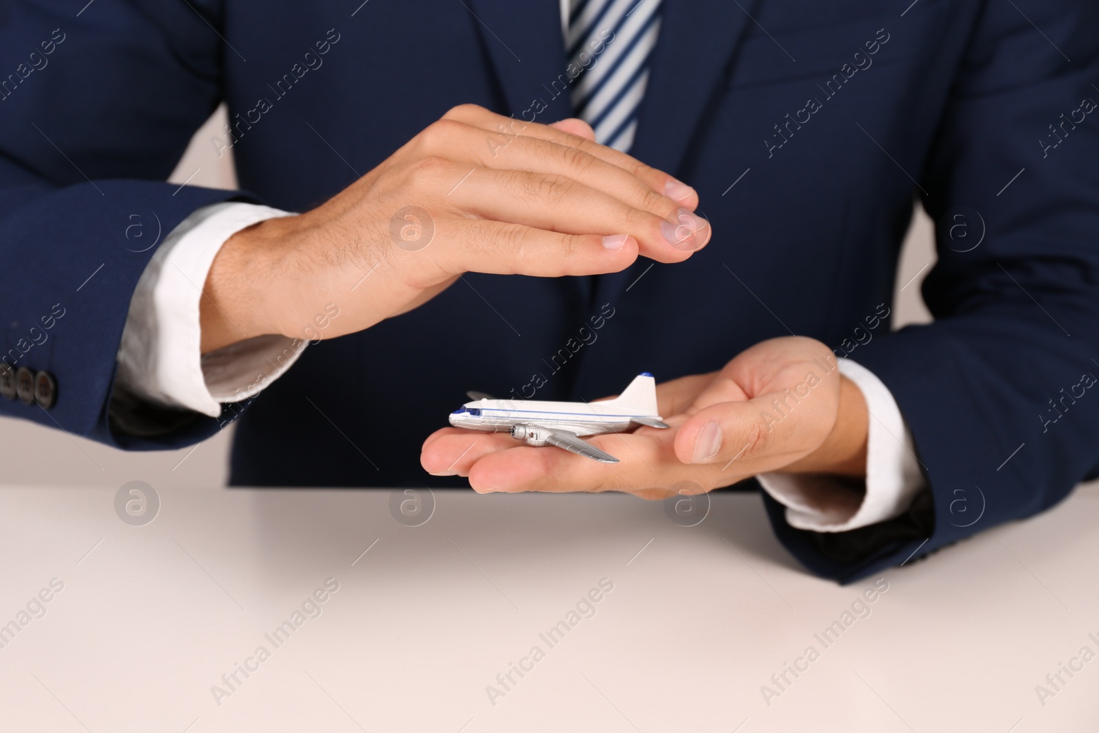 Photo of Insurance agent covering toy plane at table, closeup. Travel safety concept