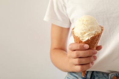 Woman holding ice cream in wafer cone on light background, closeup. Space for text