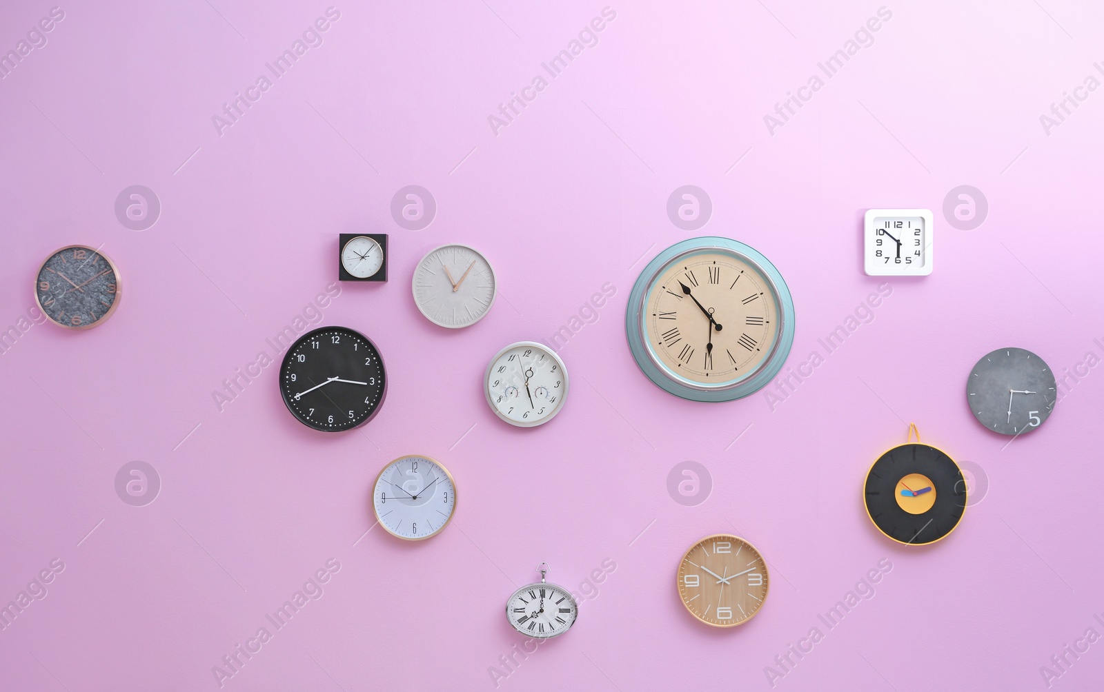 Photo of Many different clocks hanging on color wall. Time of day