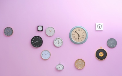 Photo of Many different clocks hanging on color wall. Time of day