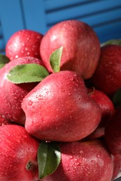 Ripe red apples with water drops and green leaves on blue background, closeup