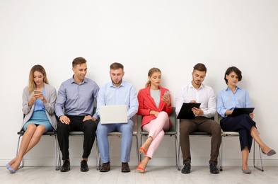 Group of young people waiting for job interview near light wall