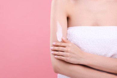 Woman with smear of body cream on her arm against pink background, closeup. Space for text
