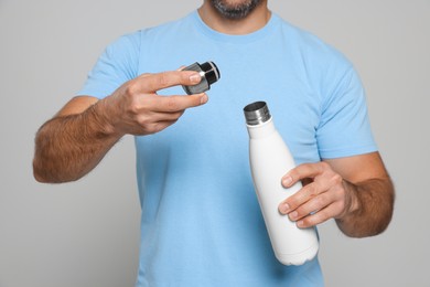 Man opening thermo bottle on light grey background, closeup