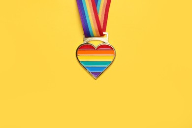 Photo of Rainbow ribbon with heart pendant on yellow background, top view and space for text. LGBT pride