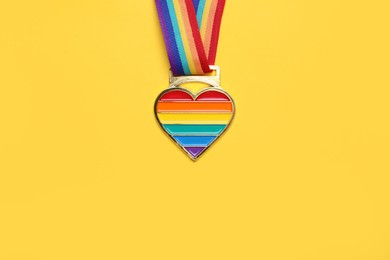 Rainbow ribbon with heart pendant on yellow background, top view and space for text. LGBT pride