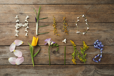 Photo of Words HELLO SPRING made of fresh flowers on wooden table, flat lay