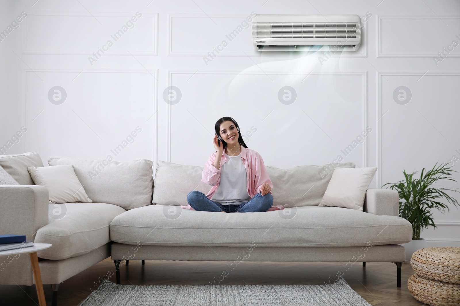 Image of Young woman resting under air conditioner on white wall at home