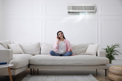 Image of Young woman resting under air conditioner on white wall at home