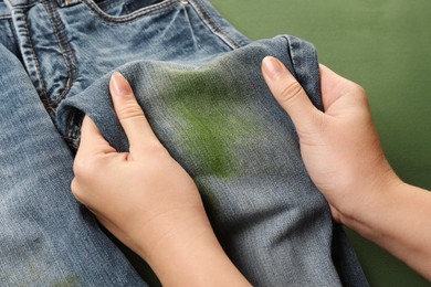 Photo of Woman holding jeans with stain on green background, closeup