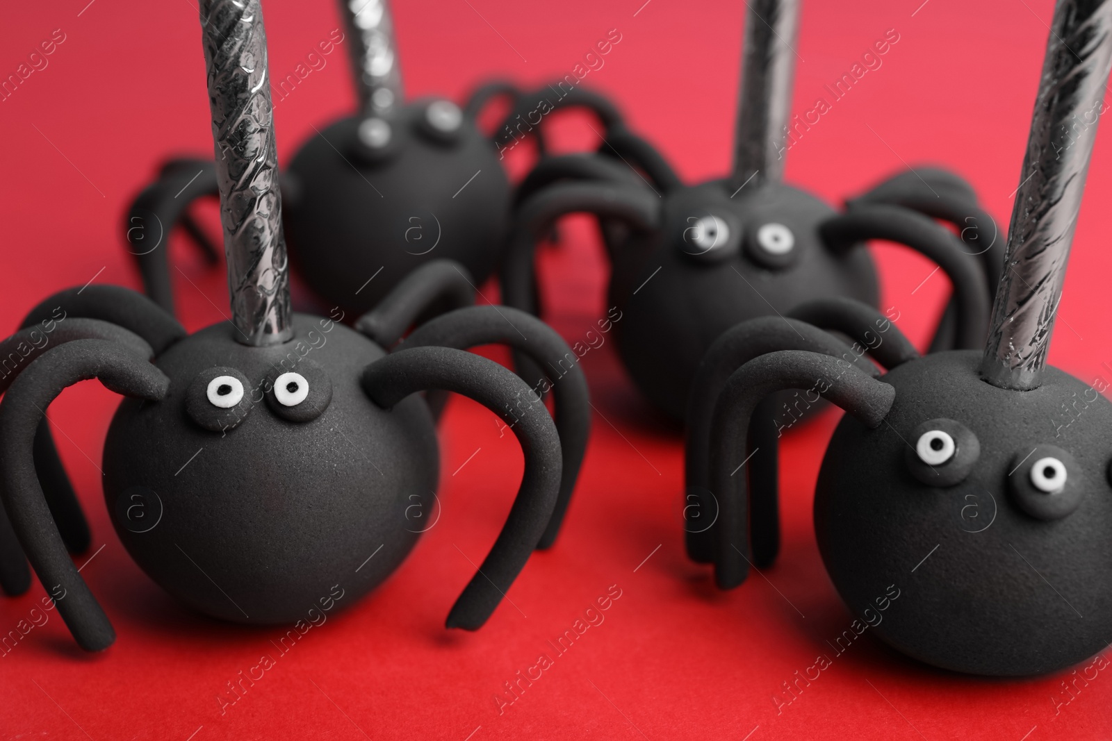 Photo of Delicious spider shaped cake pops on red background, closeup. Halloween treat