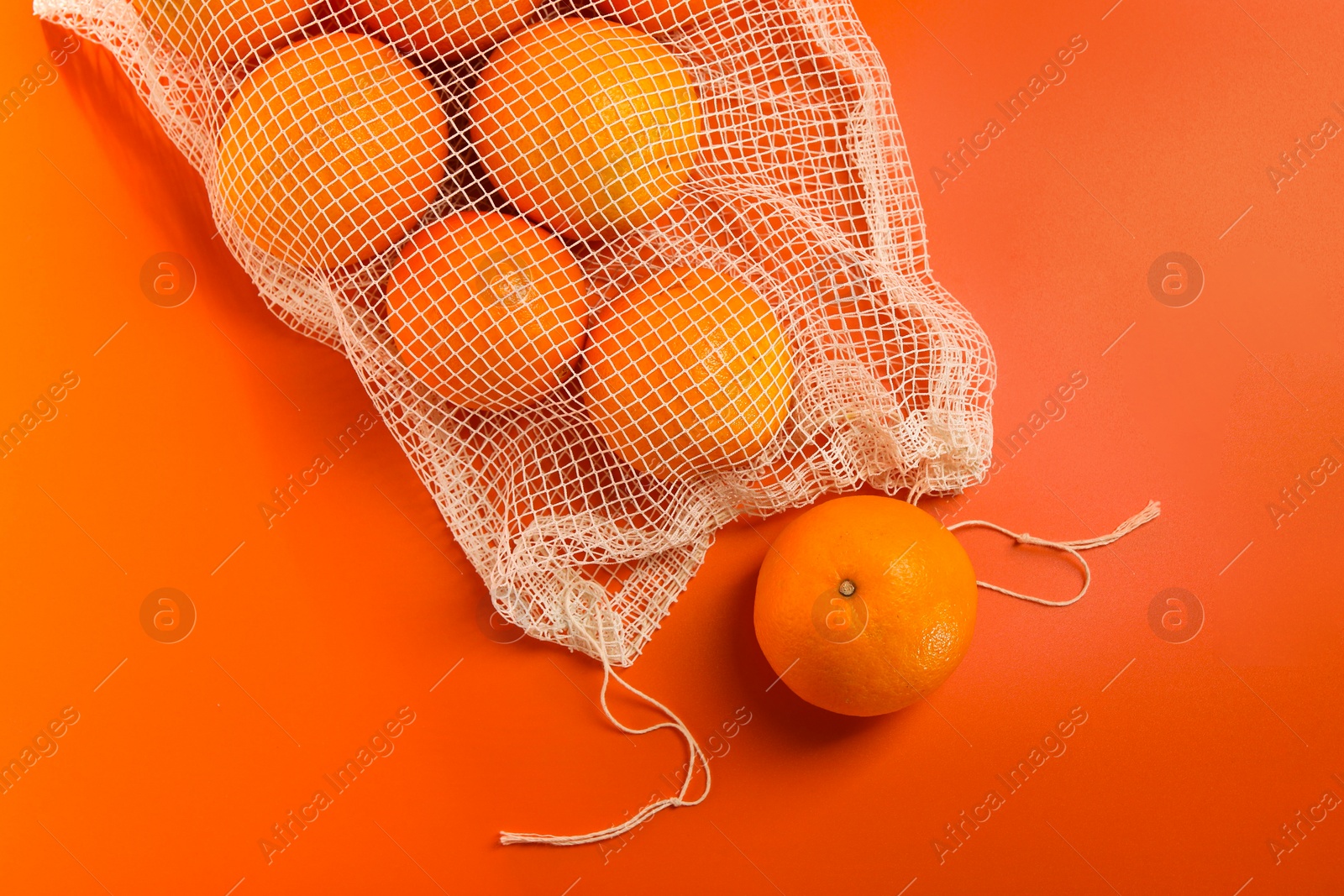 Photo of Net bag with fresh oranges on color background, top view