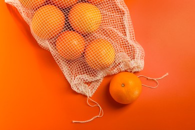 Net bag with fresh oranges on color background, top view