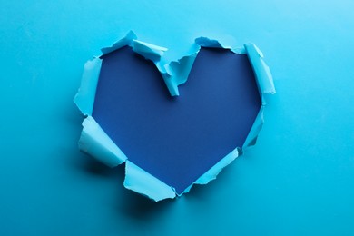 Photo of Torn heart shaped hole in light blue paper on color background